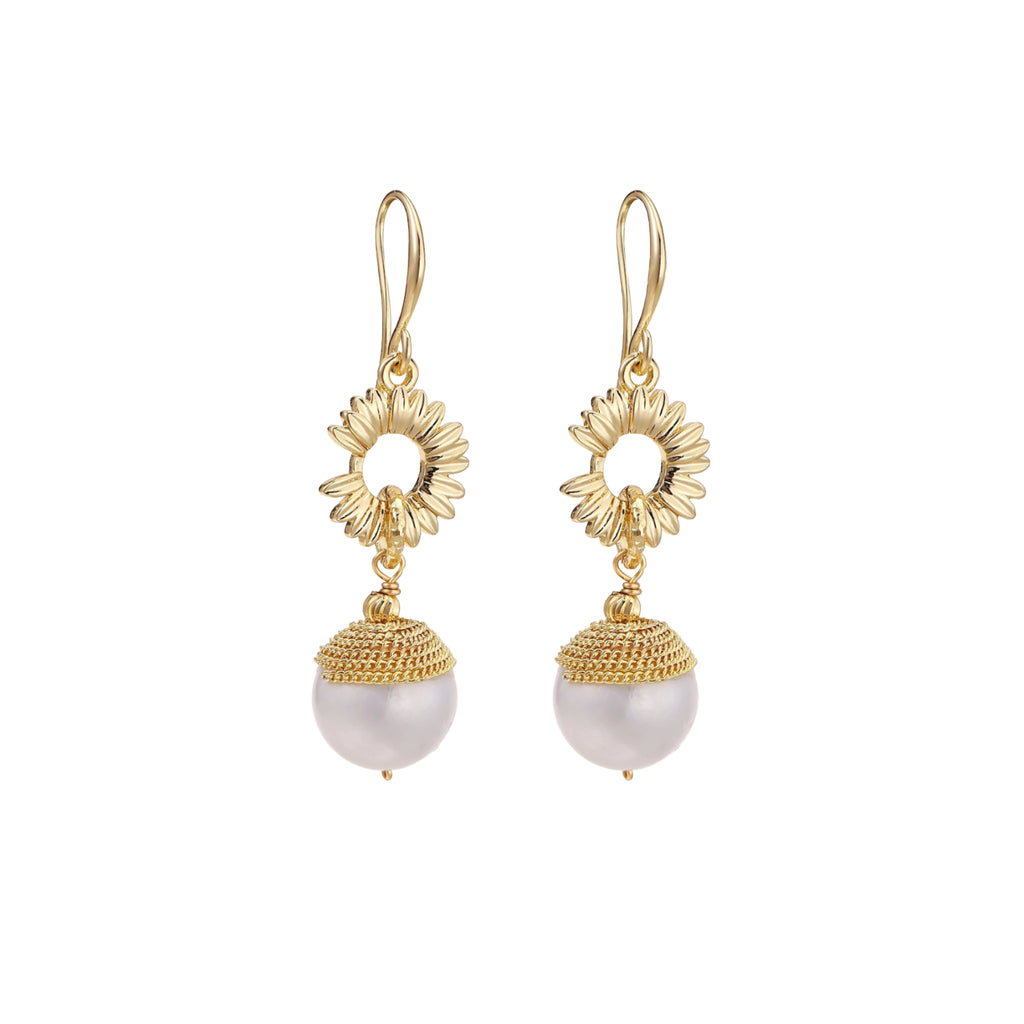 Gold sunburst charm earrings with baroque pearl drops on French hooks against cream background