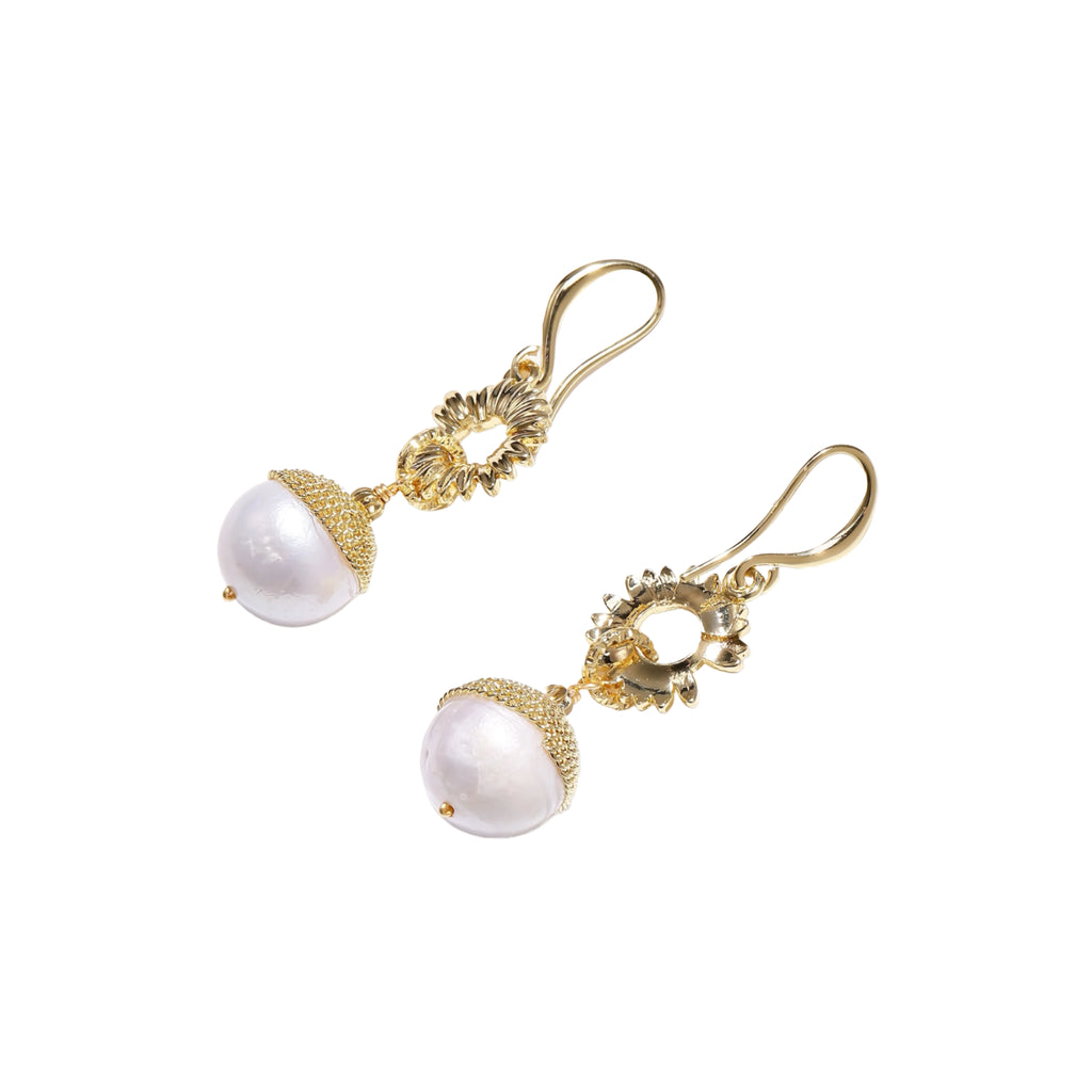 Gold sunburst charm earrings with baroque pearl drops on French hooks against cream background