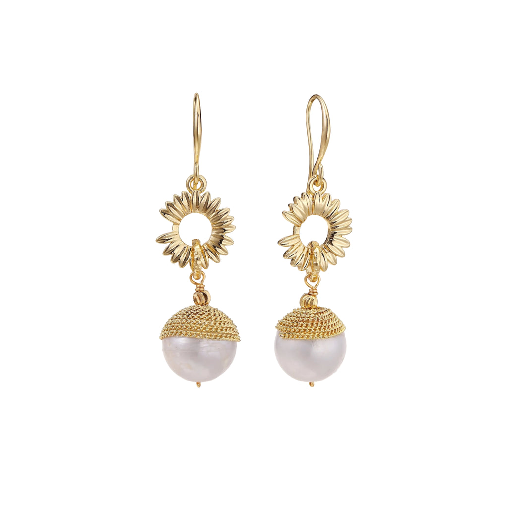 Gold sunburst charm earrings with baroque pearl drops on French hooks against cream background