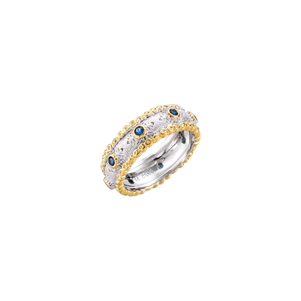 Two-tone ring with brushed silver center, gold beaded edges, and blue zirconia stones on white background.
