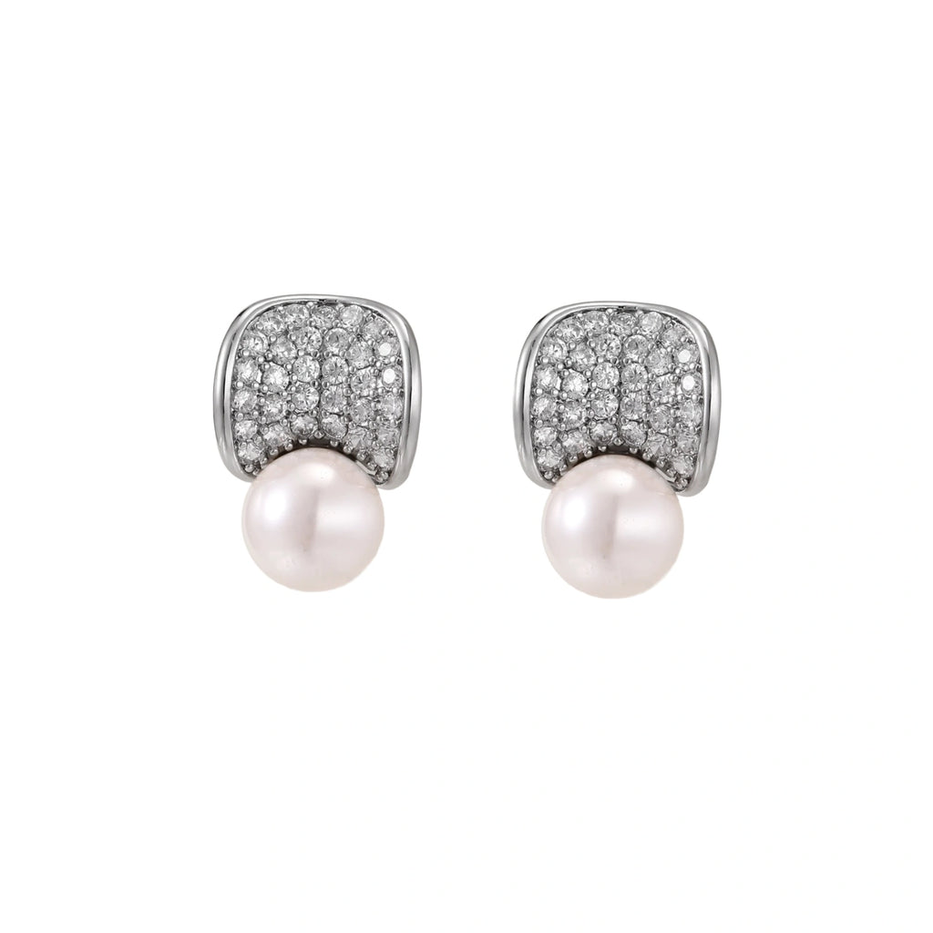 Curved pavé diamond studs in white gold-plated brass cradle lustrous freshwater pearls against cream background
