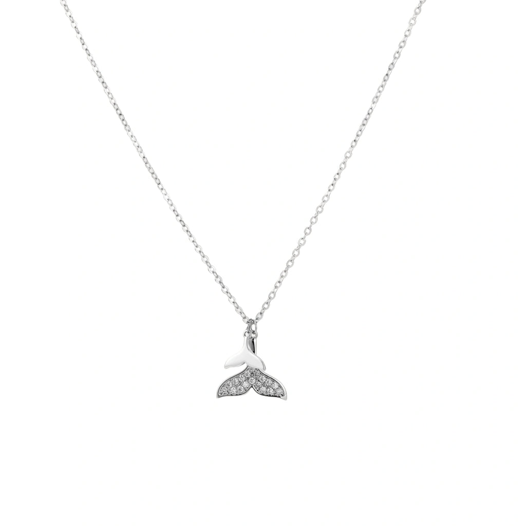 Delicate white gold plated whale tail pendant with pavé crystals on silver chain against cream background.