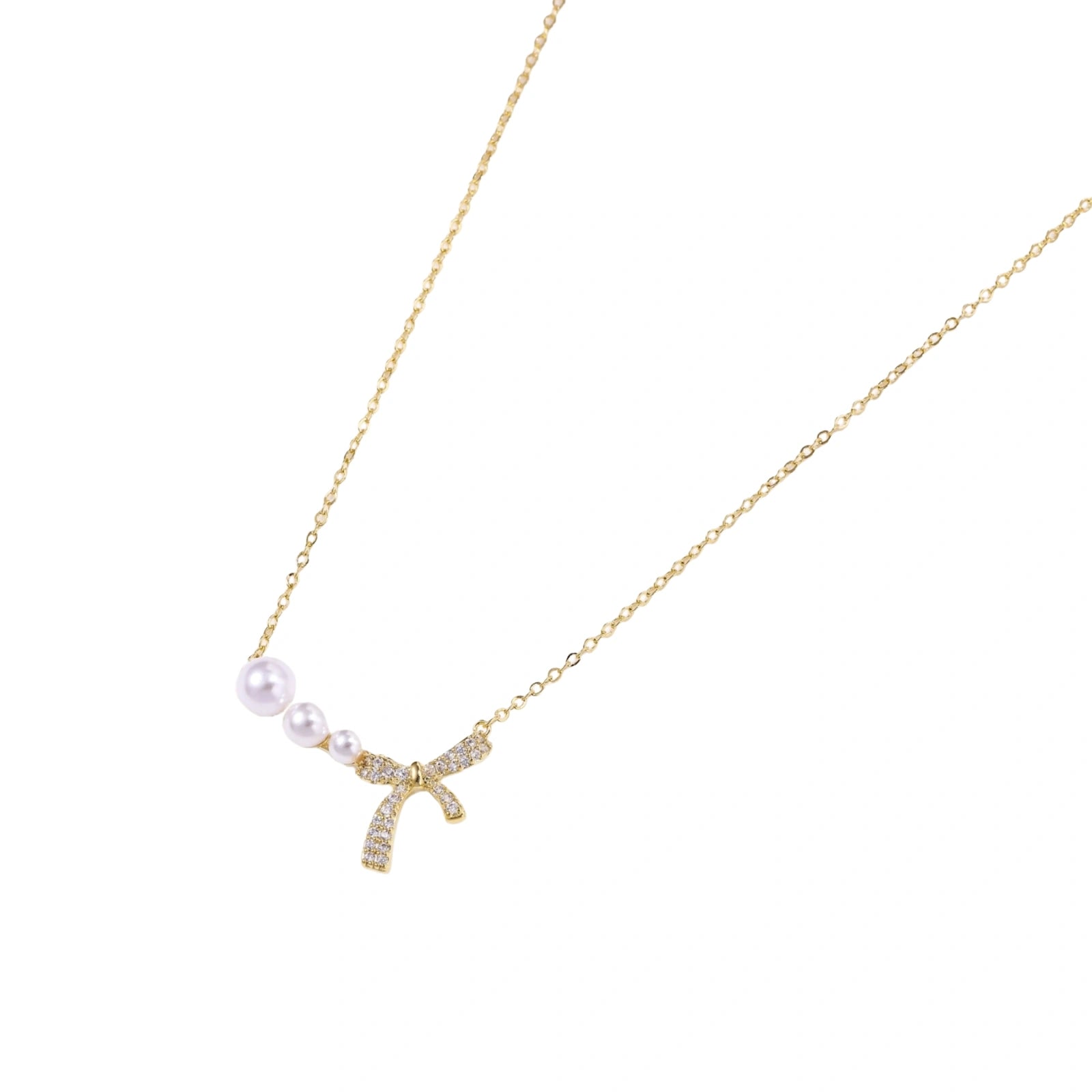 Delicate gold necklace with three white pearls and crystal-embellished bow pendant on cream background