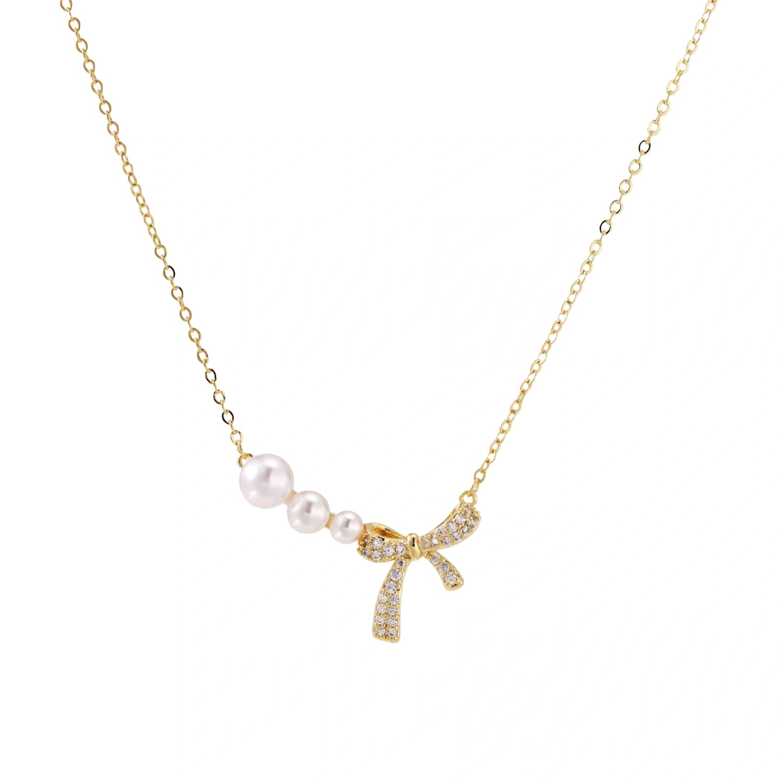 Delicate gold necklace with three white pearls and crystal-embellished bow pendant on cream background