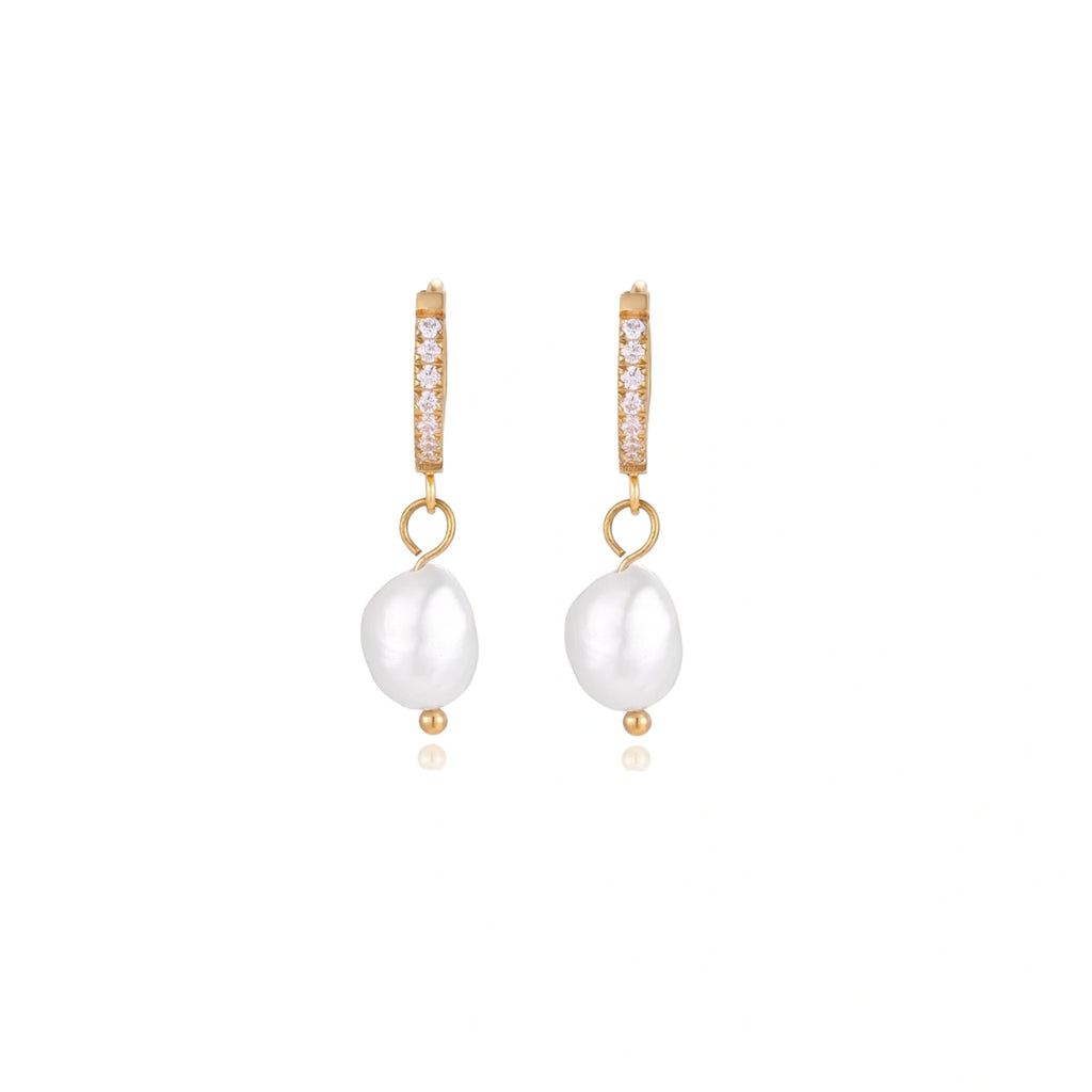 Gold huggie hoop earrings with pavé crystals and white freshwater pearl drops on cream background