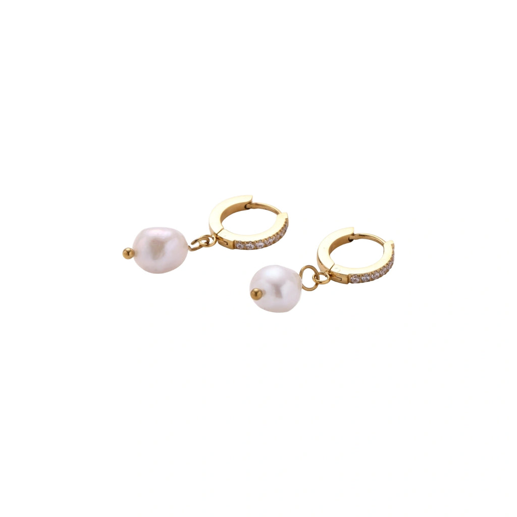 Gold huggie hoop earrings with pavé crystals and white freshwater pearl drops on cream background