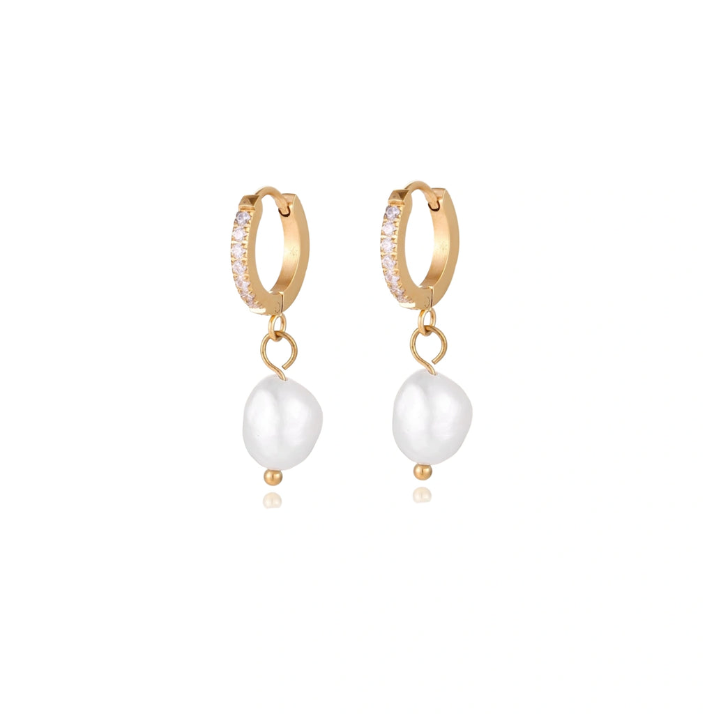 Gold huggie hoop earrings with pavé crystals and white freshwater pearl drops on cream background