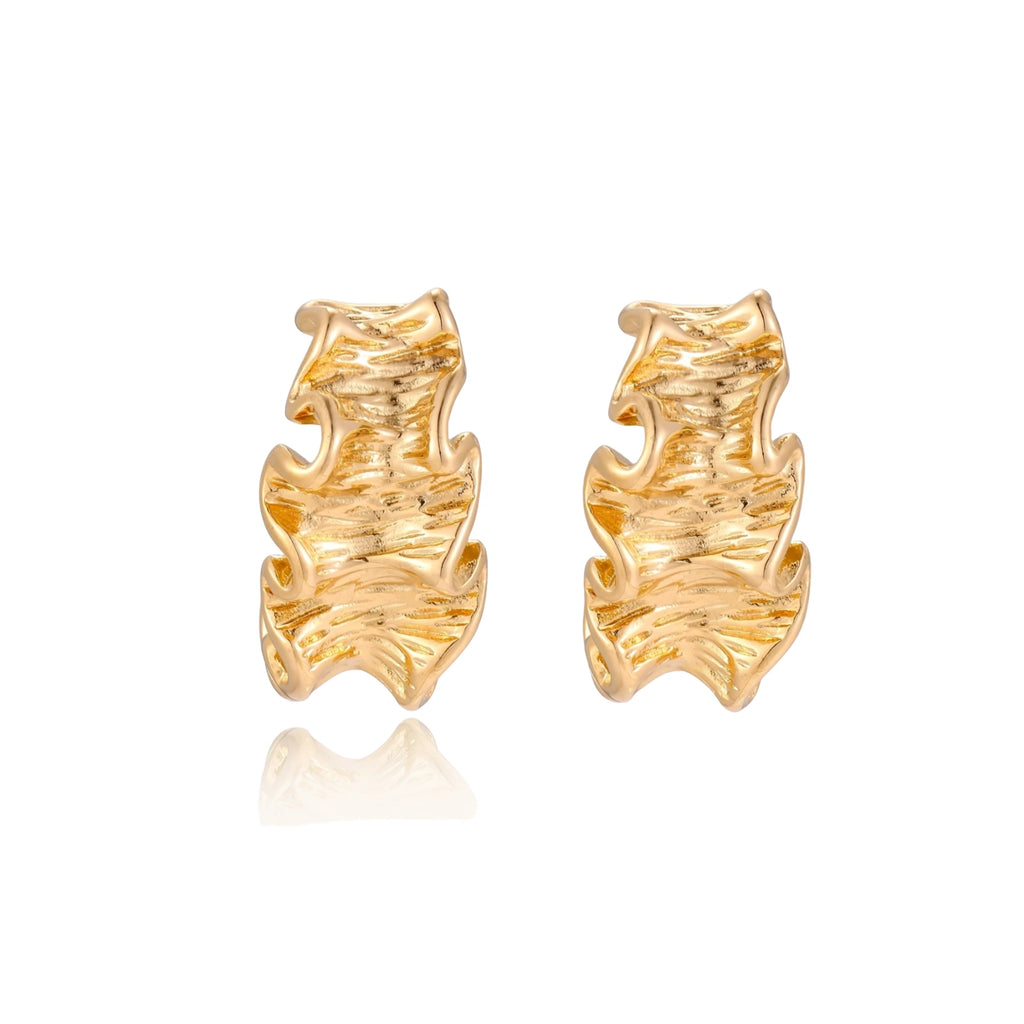 Pair of gold huggie hoops with sculpted wave texture and dimensional ripples on neutral background.