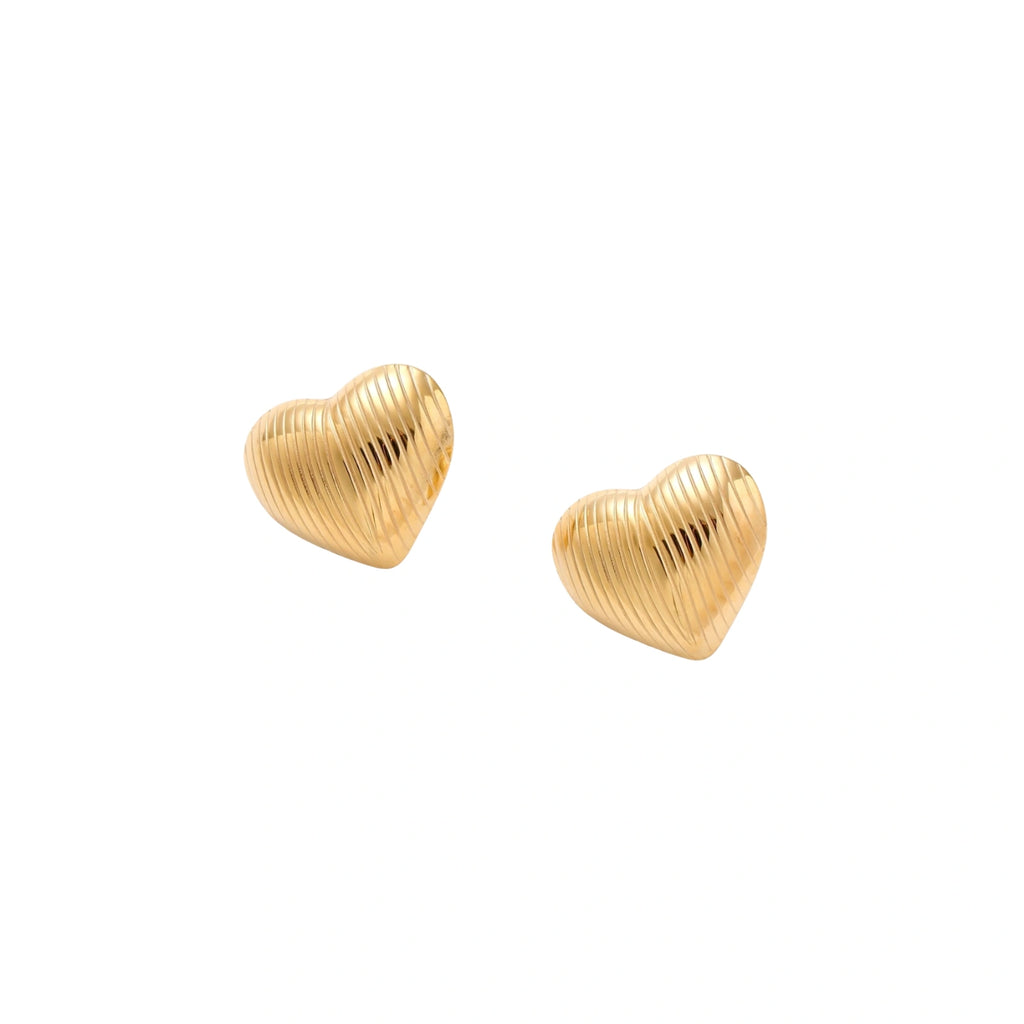 Gold heart-shaped stud earrings with parallel ridged texture on cream background