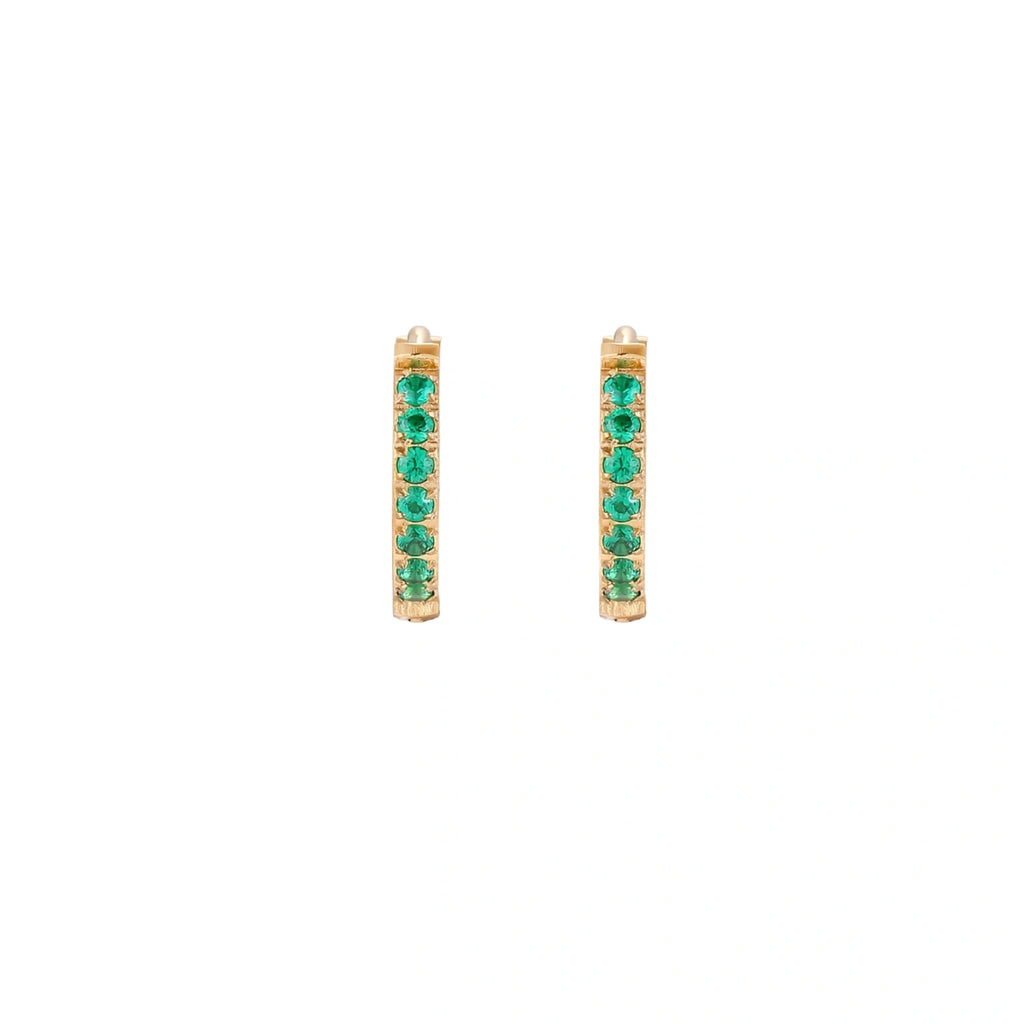 Pair of small gold huggie hoop earrings with bright green cubic zirconia stones on cream background