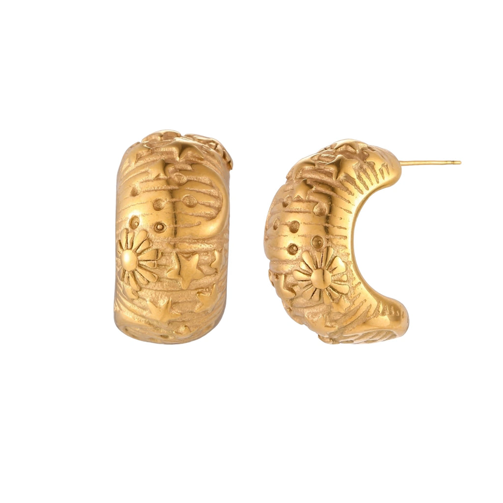 Wide gold hoop earrings with embossed stars and sun motifs on cream background, showing dimensional relief details.