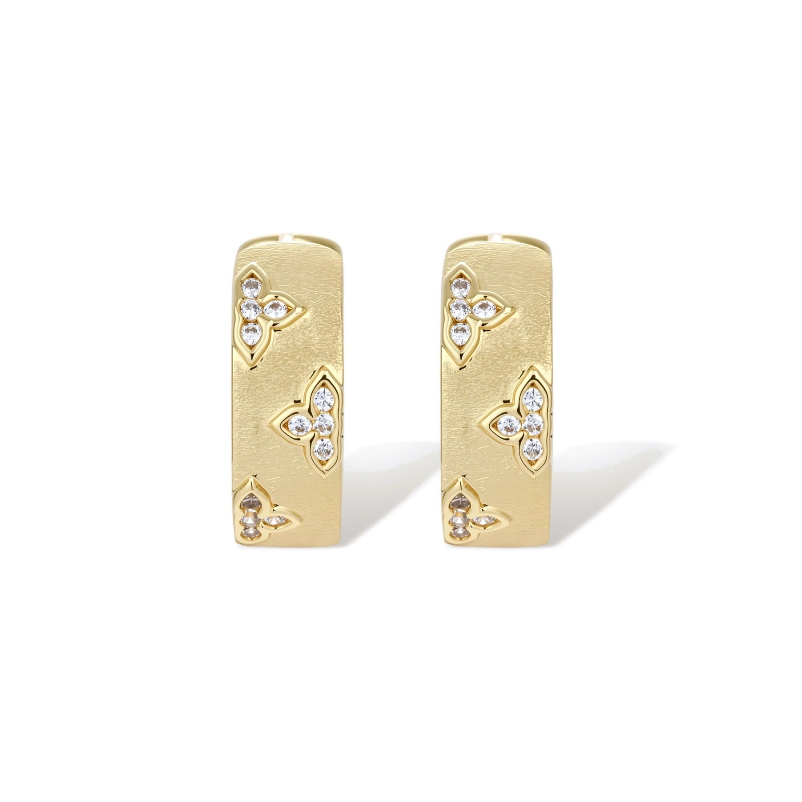 Gold-plated hoop earrings with textured surface and raised floral motifs set with clear zirconia stones on cream background.